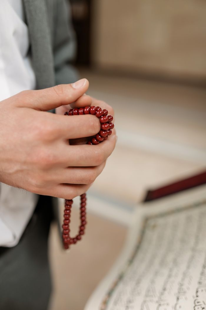 Hands holding red prayer beads near a religious text, symbolizing faith and devotion.